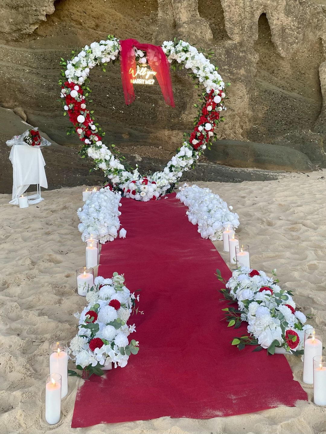 Beach ceremony aisle with red carpet and floral arch